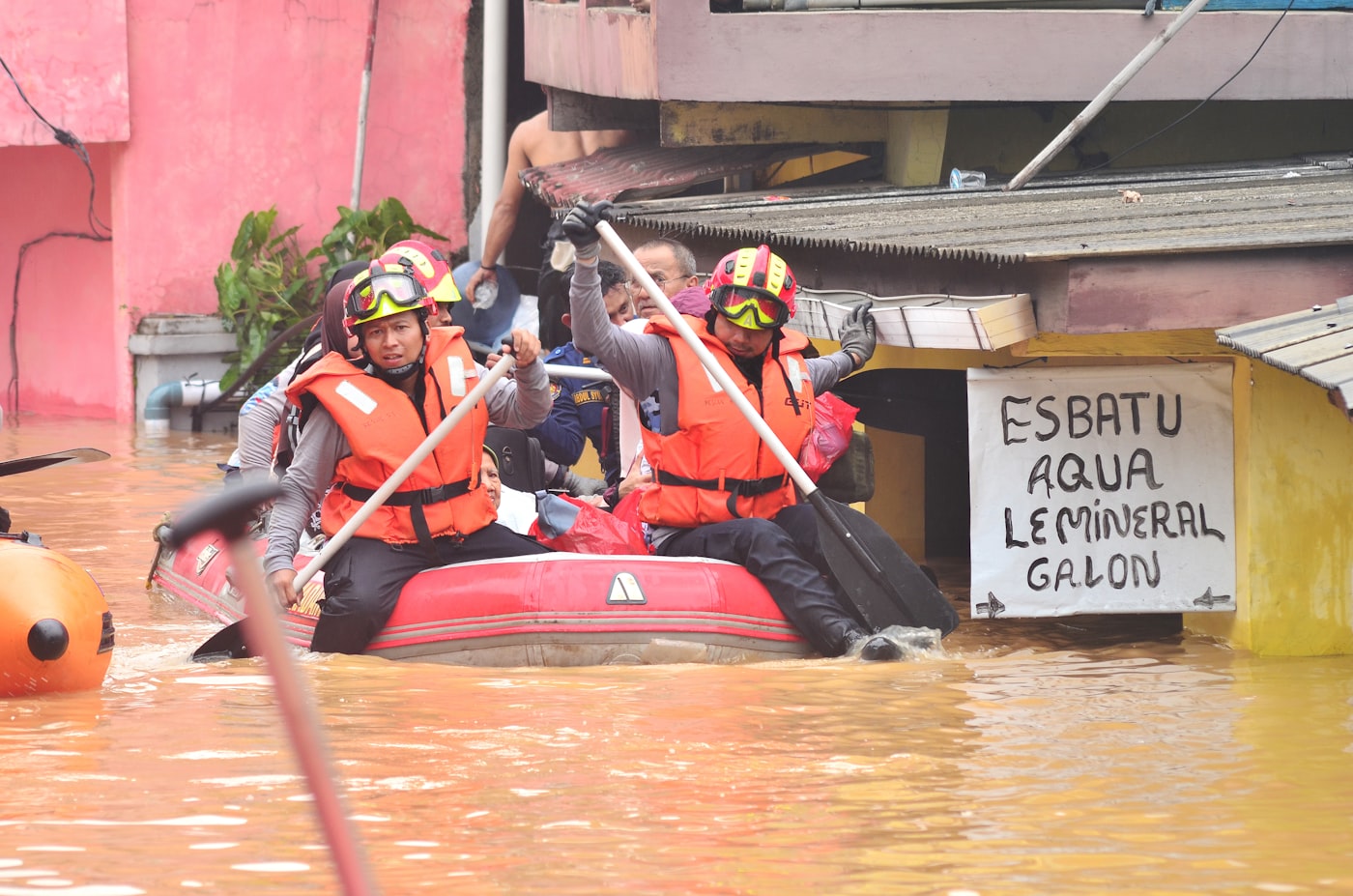 Rescue workers paddling an inflatable boat through a flooded street to reach people