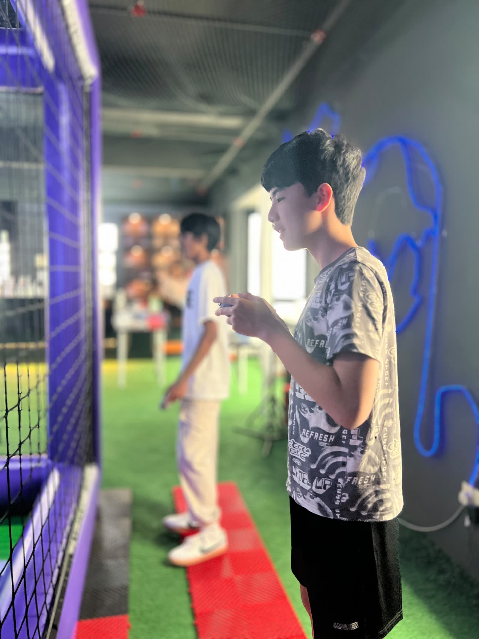 Sebastien standing at the arena netting, flying a drone with a controller