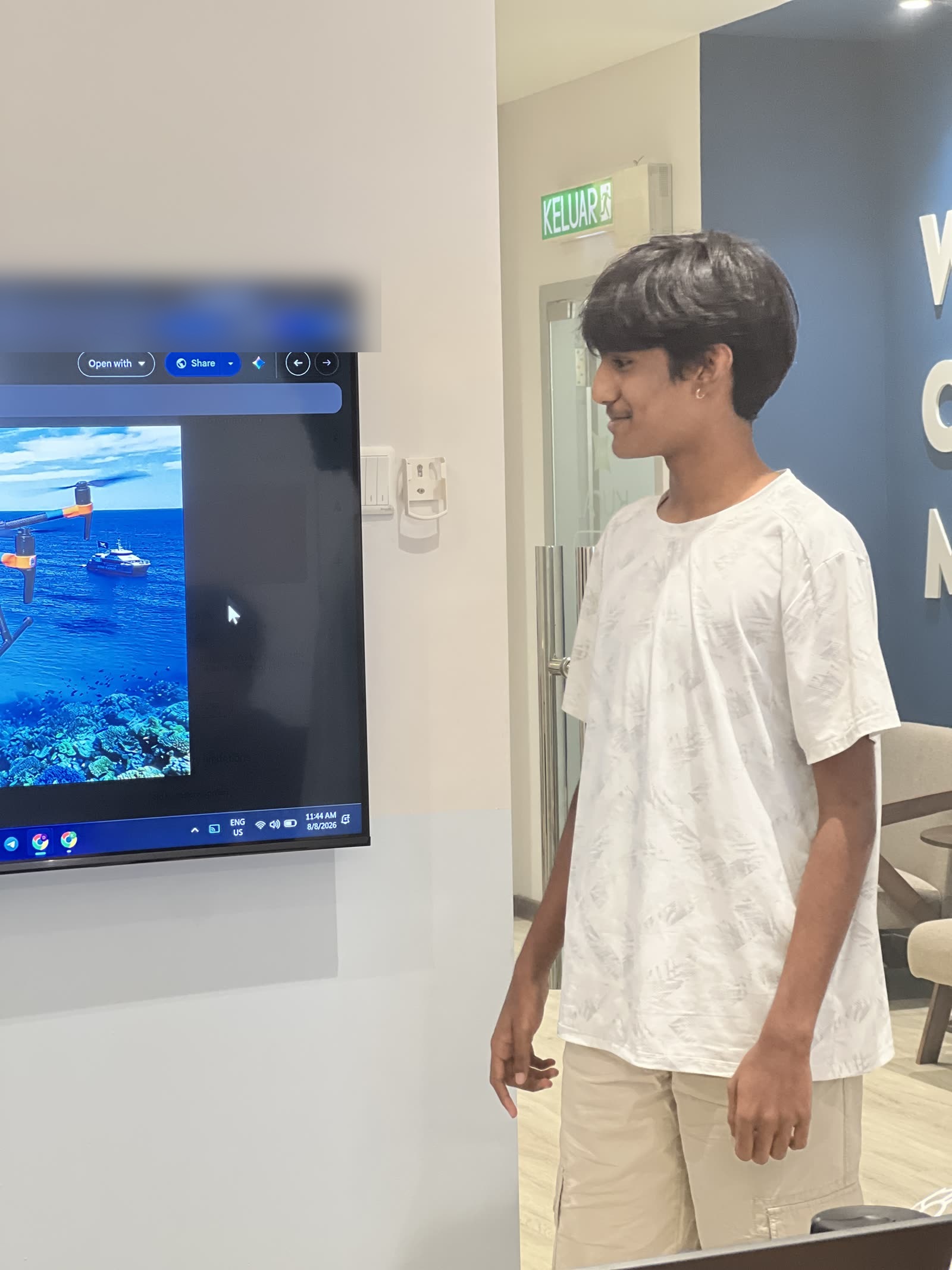 Shachin standing beside a screen showing his drone above a coral reef